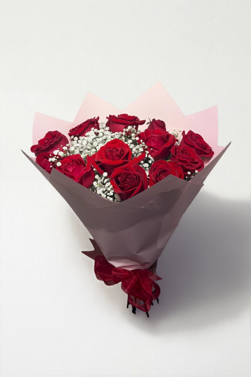Ramo de 12 rosas rojas con follaje envueltas en papel coreano coreano con moño rojo.
