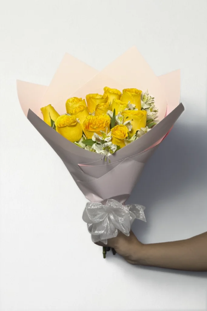 Ramo de 12 rosas amarillas con follaje envueltas en papel coreano coreano con moño rojo.