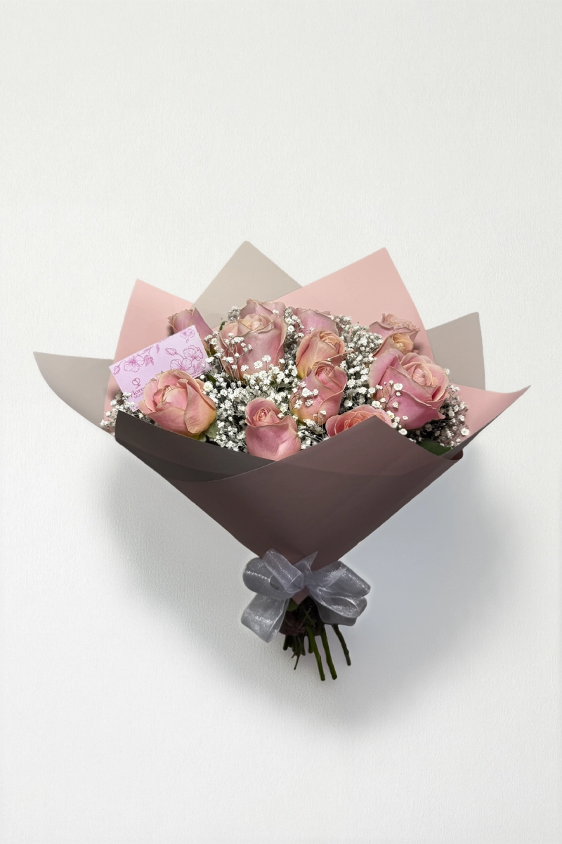 Ramo de 12 rosas rosas con follaje envueltas en papel coreano coreano con moño rojo.
