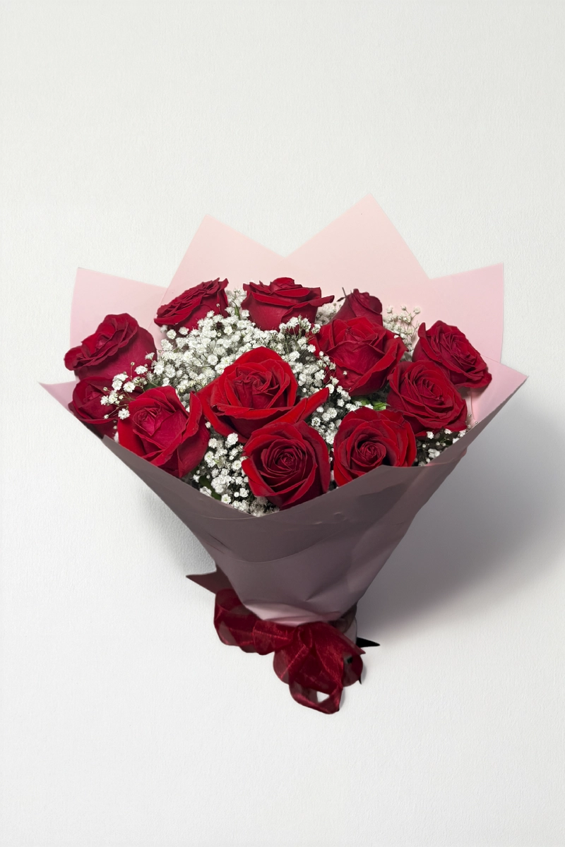 Ramo de 12 rosas rojas con follaje envueltas en papel coreano coreano con moño rojo.