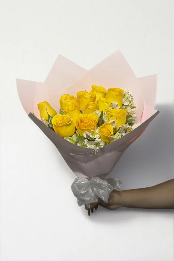 Ramo de 12 rosas amarillas con follaje envueltas en papel coreano coreano con moño rojo.