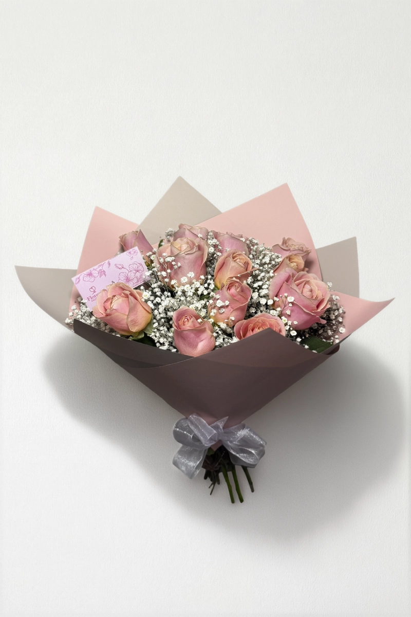 Ramo de 12 rosas rosas con follaje envueltas en papel coreano coreano con moño rojo.