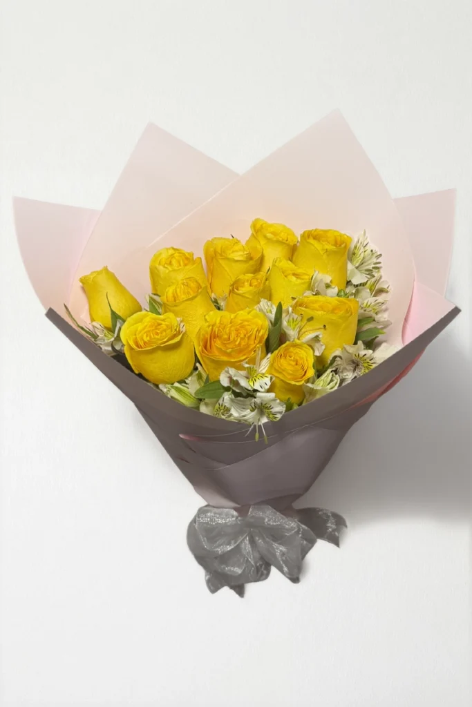 Ramo de 12 rosas amarillas con follaje envueltas en papel coreano coreano con moño rojo.