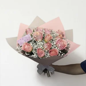 Ramo de 12 rosas rosas con follaje envueltas en papel coreano coreano con moño rojo.