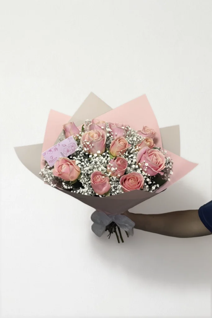 Ramo de 12 rosas rosas con follaje envueltas en papel coreano coreano con moño rojo.