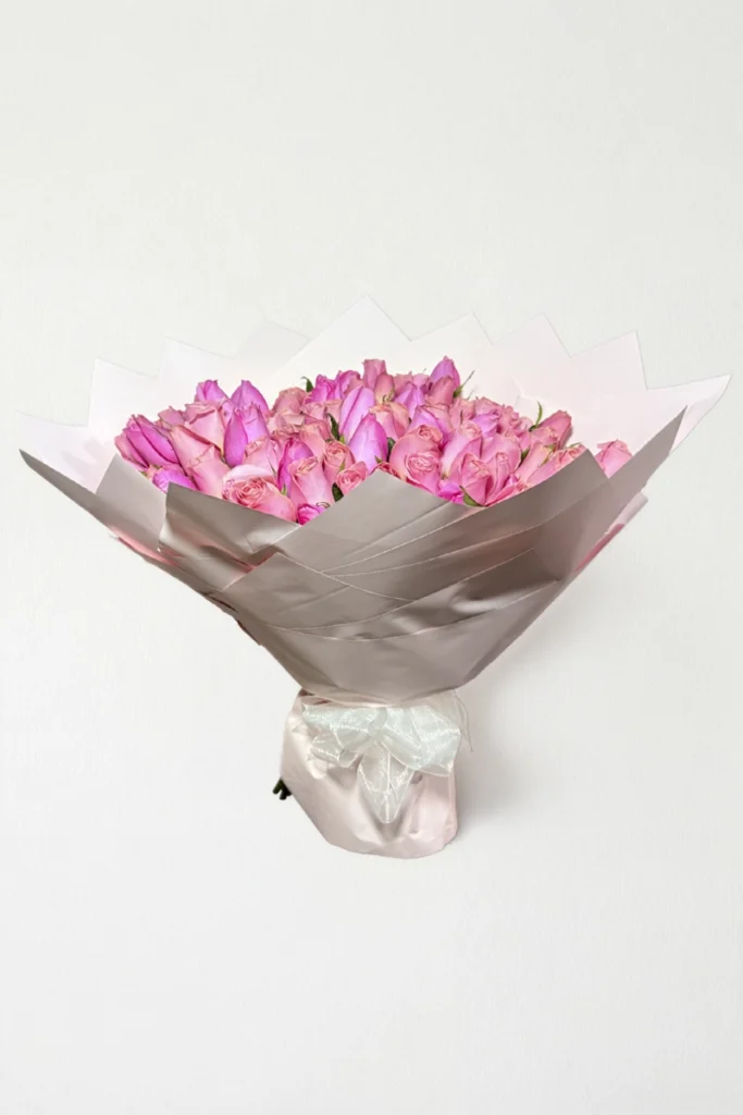 Ramo de 100 rosas rosas con follaje envueltas en papel coreano con moño.