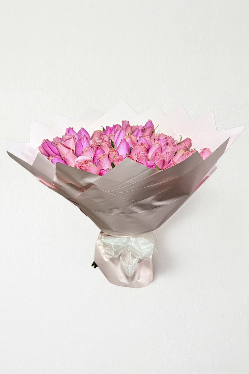 Ramo de 100 rosas rosas con follaje envueltas en papel coreano con moño.