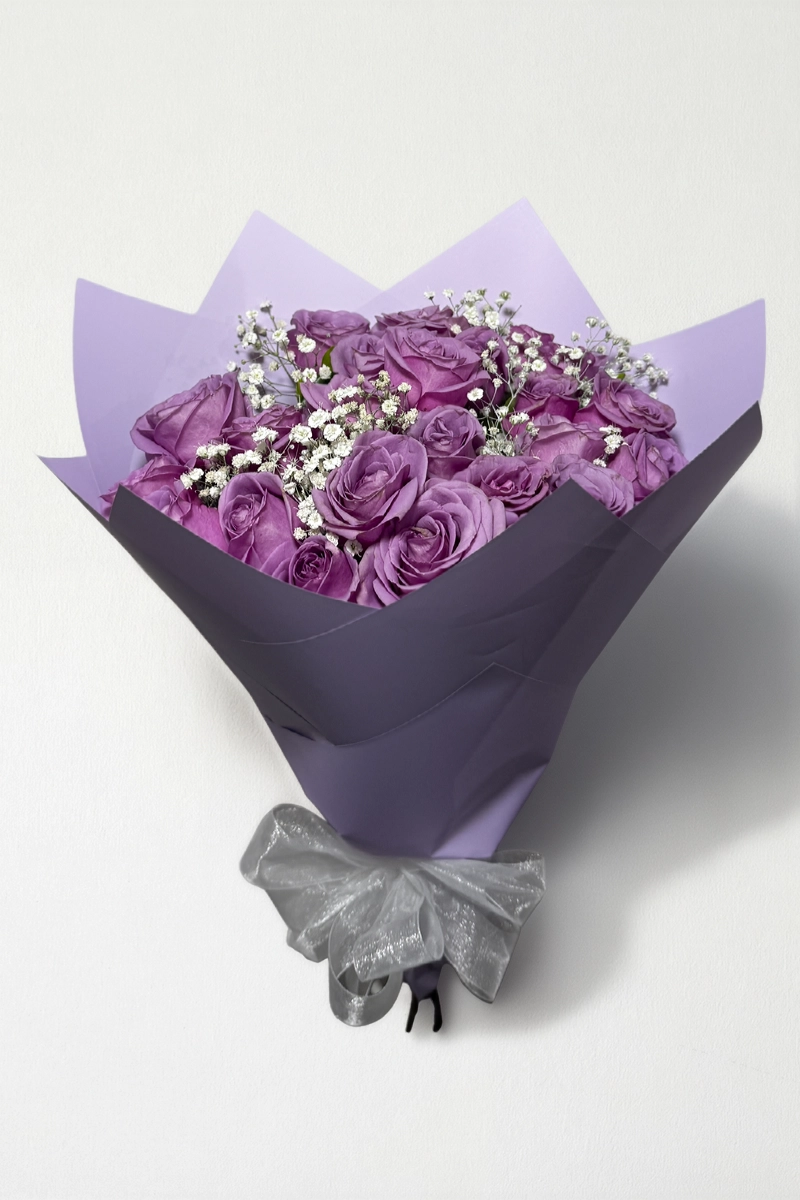 Ramo de 24 rosas lila con follaje envueltas en papel coreano con moño.