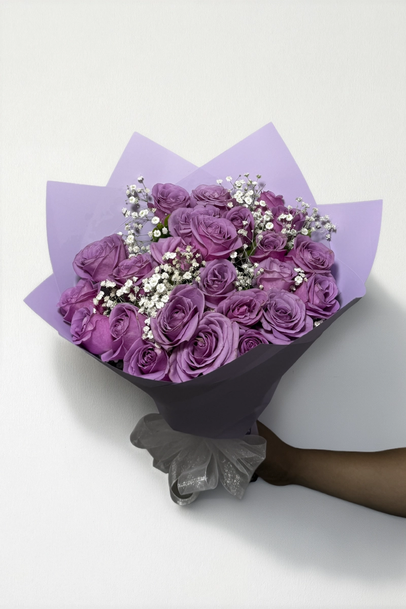 Ramo de 24 rosas lila con follaje envueltas en papel coreano con moño.
