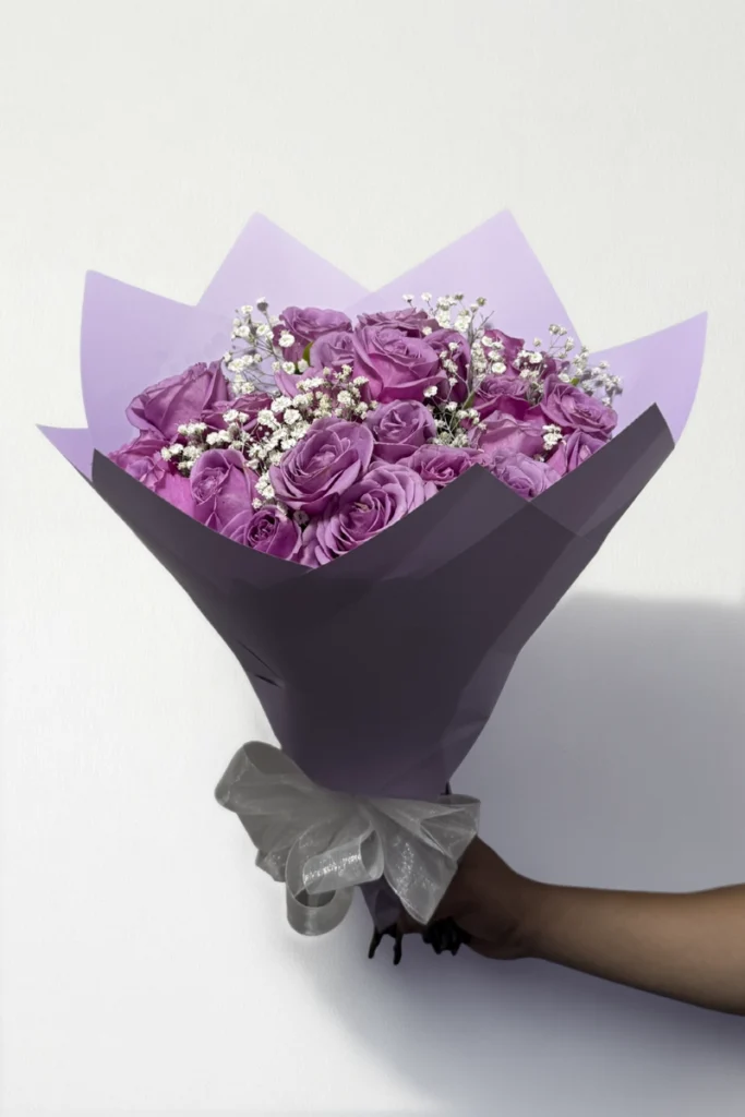 Ramo de 24 rosas lila con follaje envueltas en papel coreano con moño.