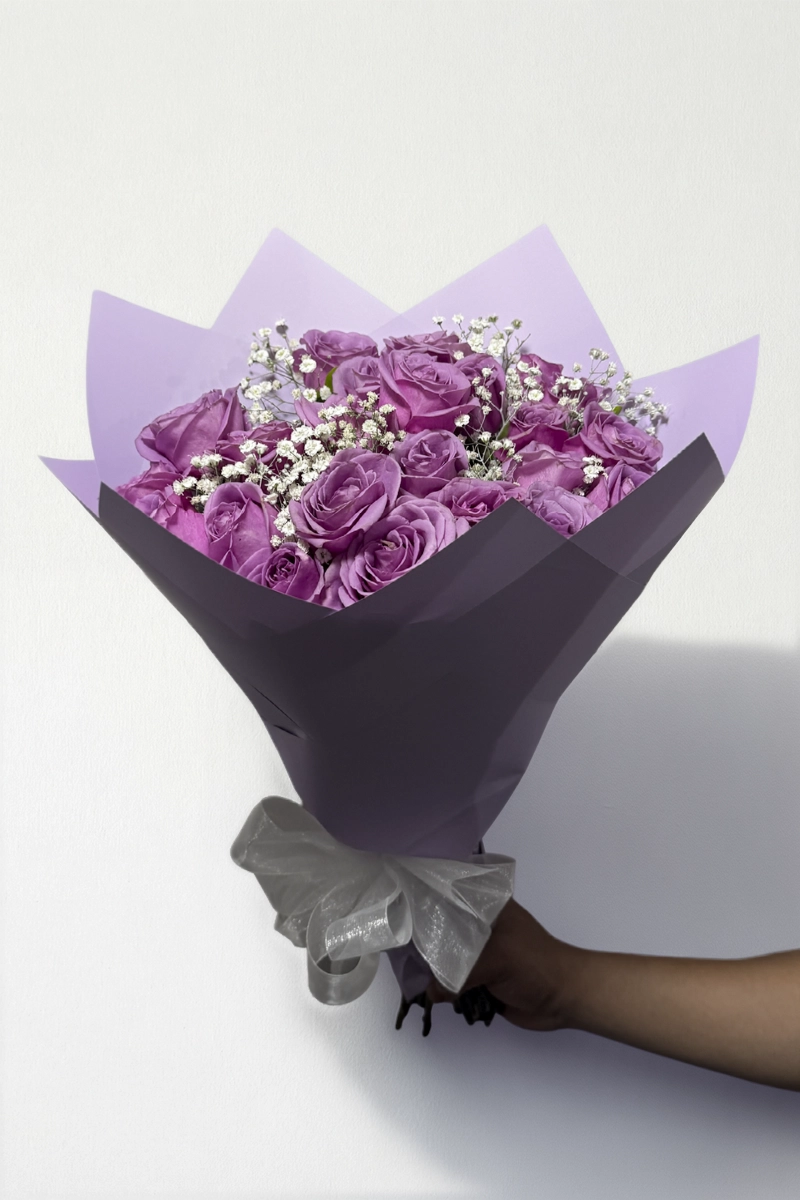 Ramo de 24 rosas lila con follaje envueltas en papel coreano con moño.