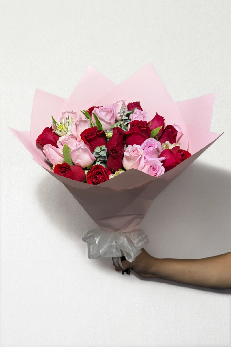 Ramo de 24 rosas rojas y rosas con follaje envueltas en papel coreano con moño.