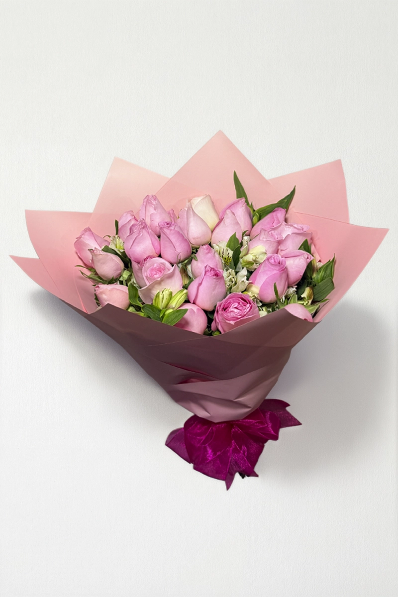 Ramo de 24 rosas rosas con follaje envueltas en papel coreano con moño.