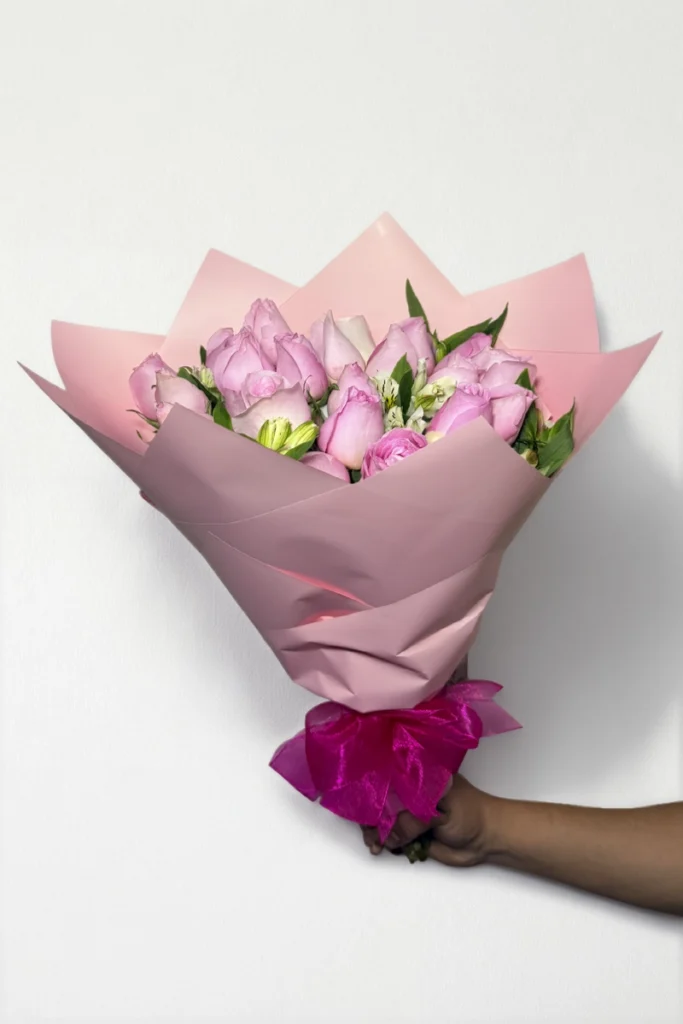 Ramo de 24 rosas rosas con follaje envueltas en papel coreano con moño.