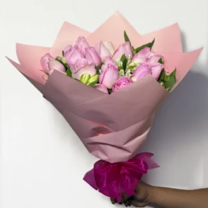 Ramo de 24 rosas rosas con follaje envueltas en papel coreano con moño.