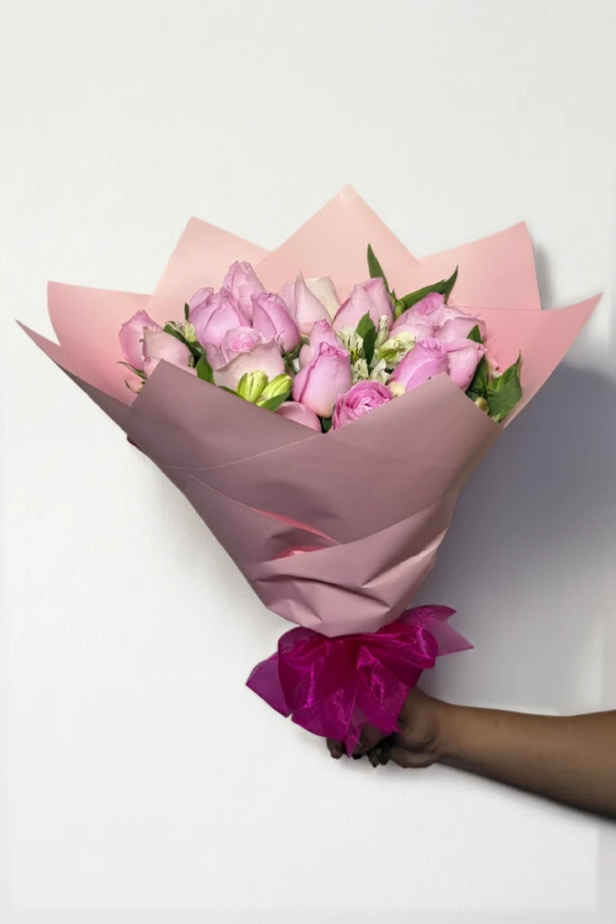 Ramo de 24 rosas rosas con follaje envueltas en papel coreano con moño.