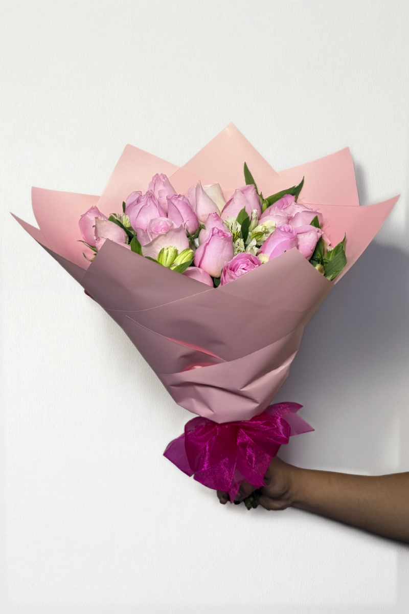 Ramo de 24 rosas rosas con follaje envueltas en papel coreano con moño.