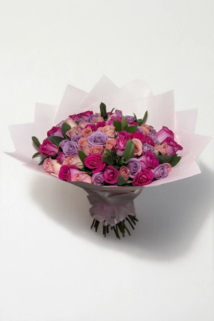 Ramo de 50 rosas lila, rosa y fucsia con follaje envueltas en papel coreano con moño.