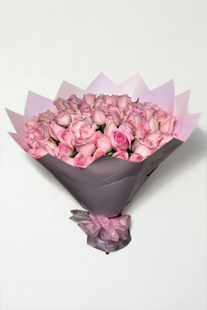 Ramo de 50 rosas rosas con follaje envueltas en papel coreano con moño.