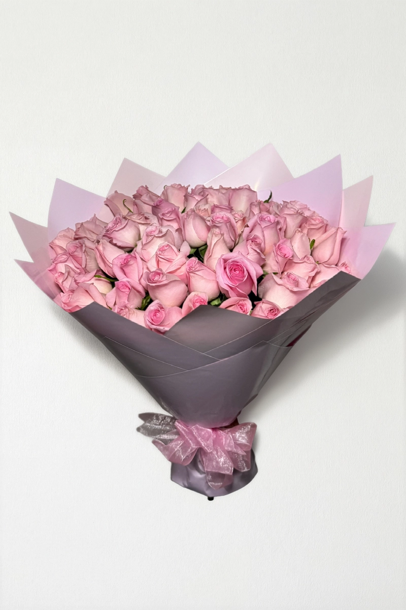 Ramo de 50 rosas rosas con follaje envueltas en papel coreano con moño.